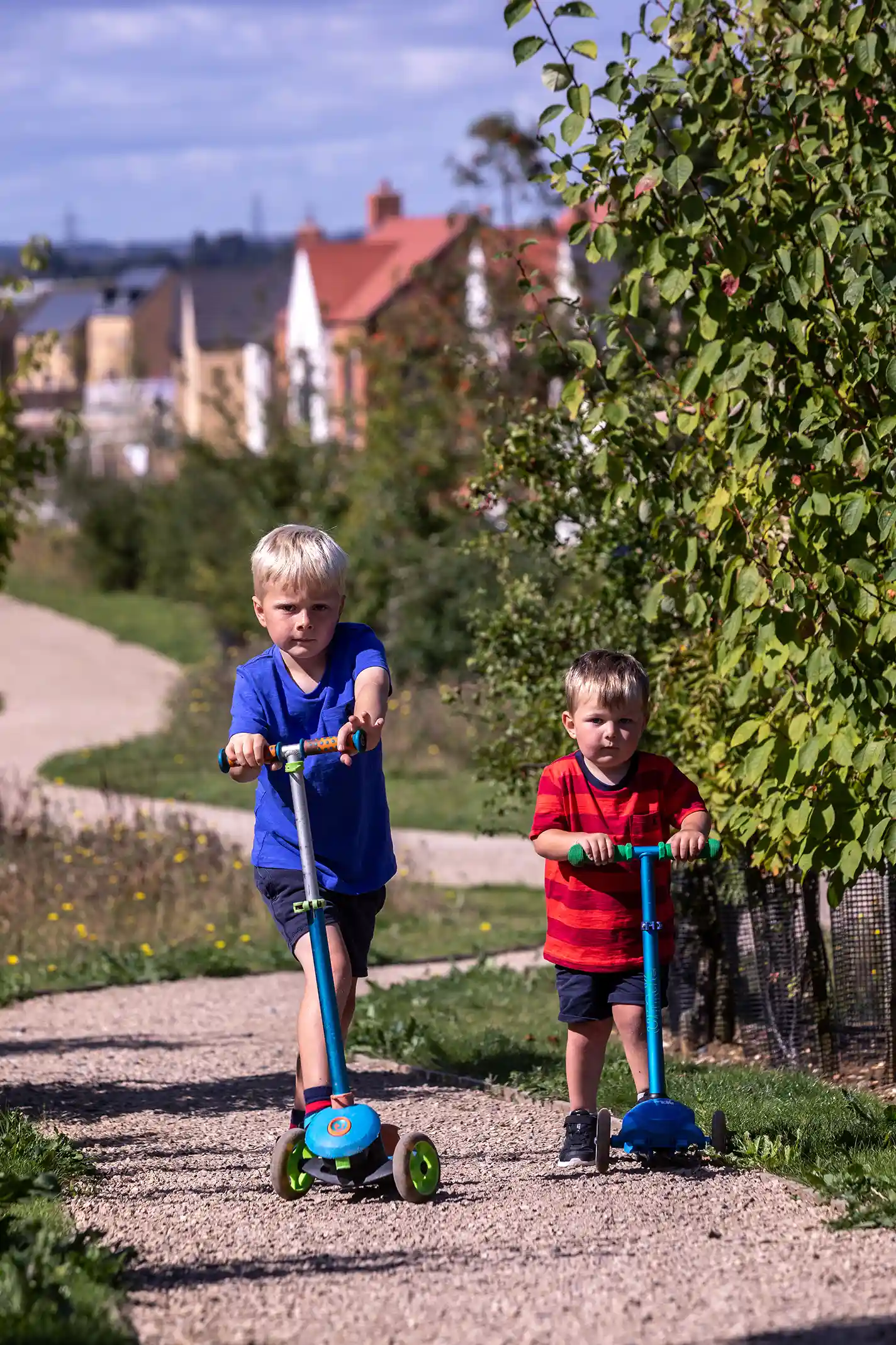 Two toddlers on scooters, riding along a path 
