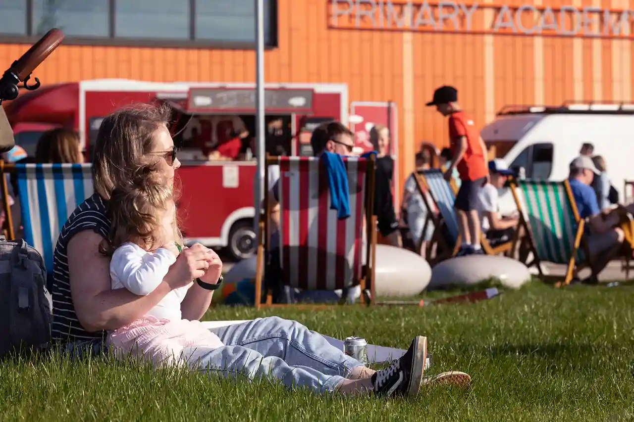 Mother and child sitting on the grass with food vans in the background