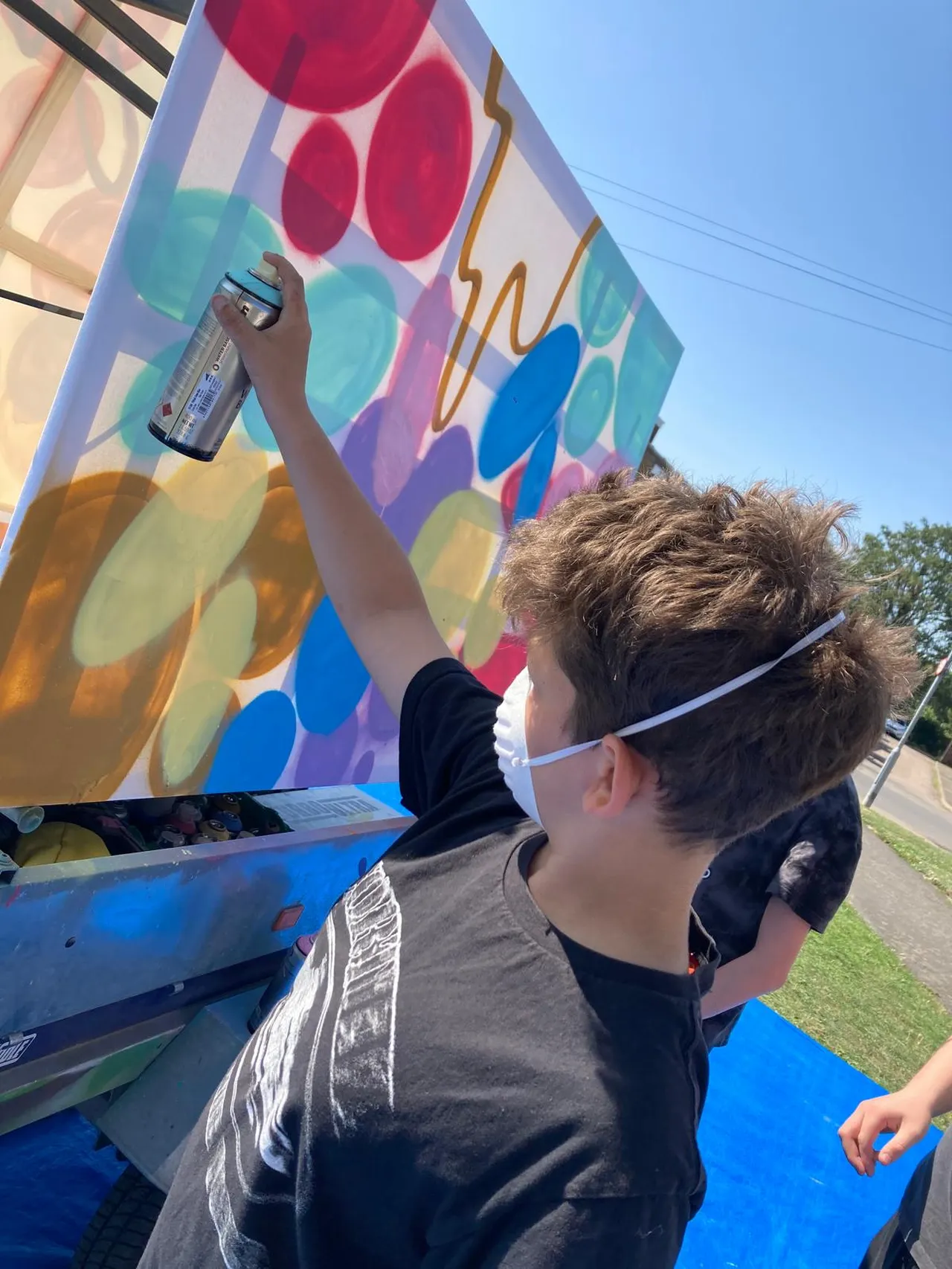 A vibrant, multi-colored spray-painted mural created by young people and a local graffiti artist in St Neots, featuring bold graffiti lettering, abstract patterns, and community-themed designs.