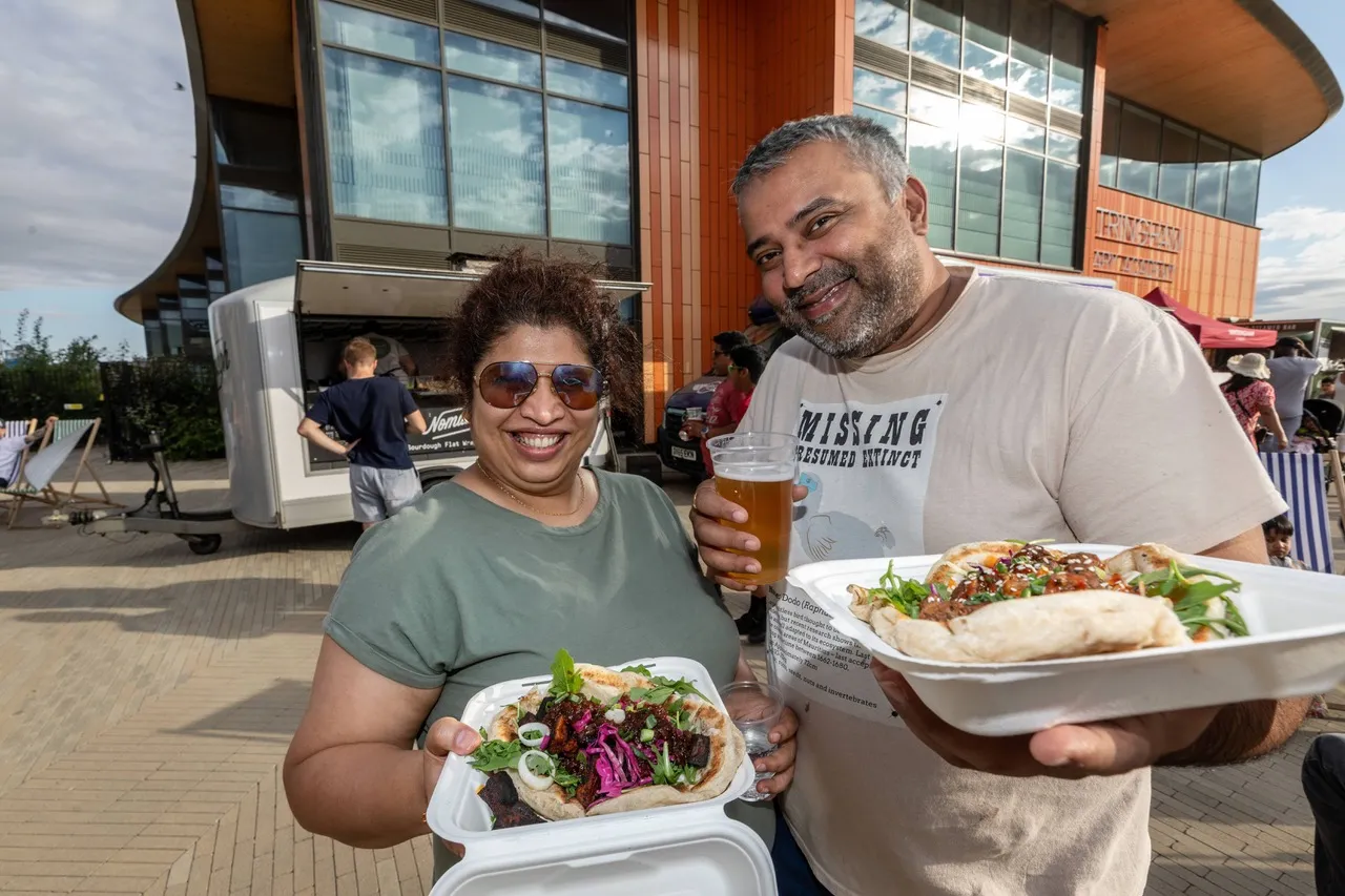 wo smiling people hold fresh sourdough flatbread wraps and drinks as Wintringham enjoys taste of summer at pop-up street food event outside Wintringham Primary Academy.