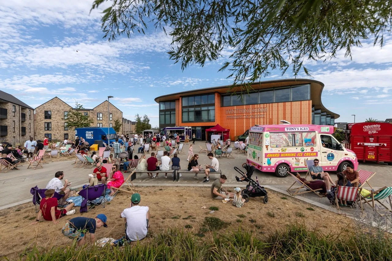 Wide shot of community members relaxing in deckchairs surrounded by food trucks outside Wintringham Primary Academy as Wintringham enjoys taste of summer at pop-up street food event.